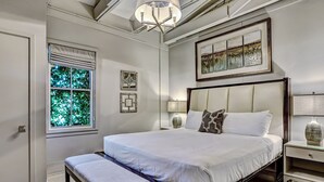 A neatly arranged bedroom with a large bed, a bench, a bedside table with a lamp, and a window with blinds. - Modern Interior, Heated Pool Access (Savannah)