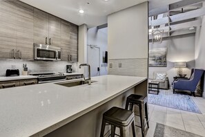 A modern kitchen with a large island, stainless steel appliances, and a dining area with a blue chair and a sofa.