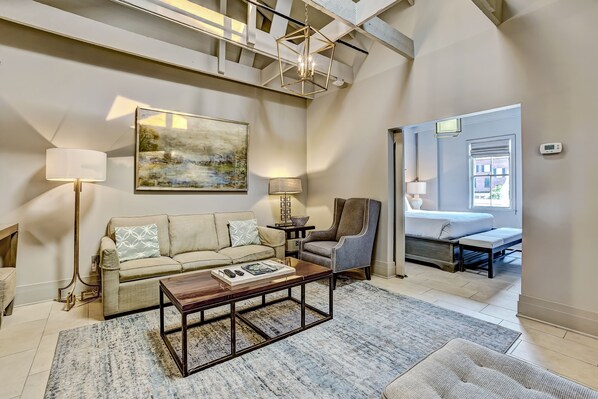A modern living room with a sofa, armchair, coffee table, and artwork on the wall. - Modern Interior, Heated Pool Access (Savannah)