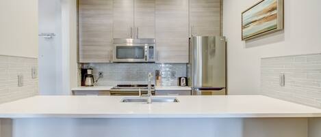 A modern kitchen with stainless steel appliances, a white countertop, and a tiled backsplash.