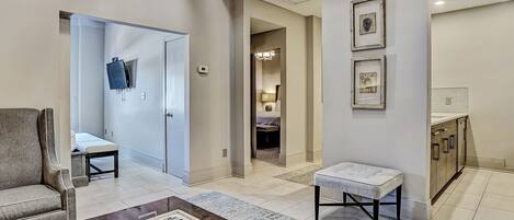 Una sala de estar moderna con un sofá, una mesa de centro con controles remotos, un televisor y un pasillo que lleva a un dormitorio.
