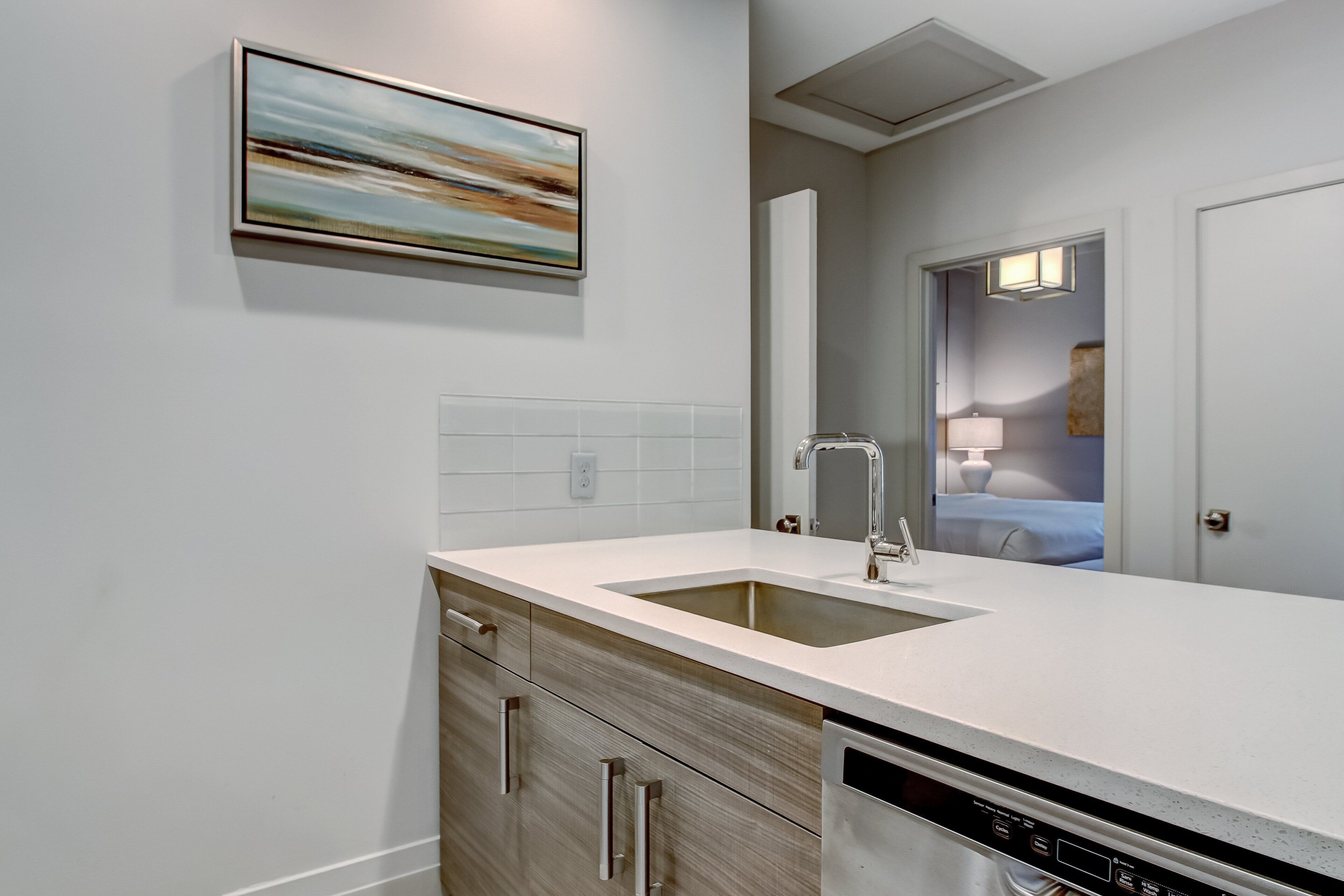 A modern kitchen with a white countertop, stainless steel sink, and wooden cabinets.