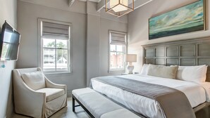 A modern bedroom with a large bed, a chair, a bench, a TV, and two windows. - Modern Interior, Heated Pool Access (Savannah)