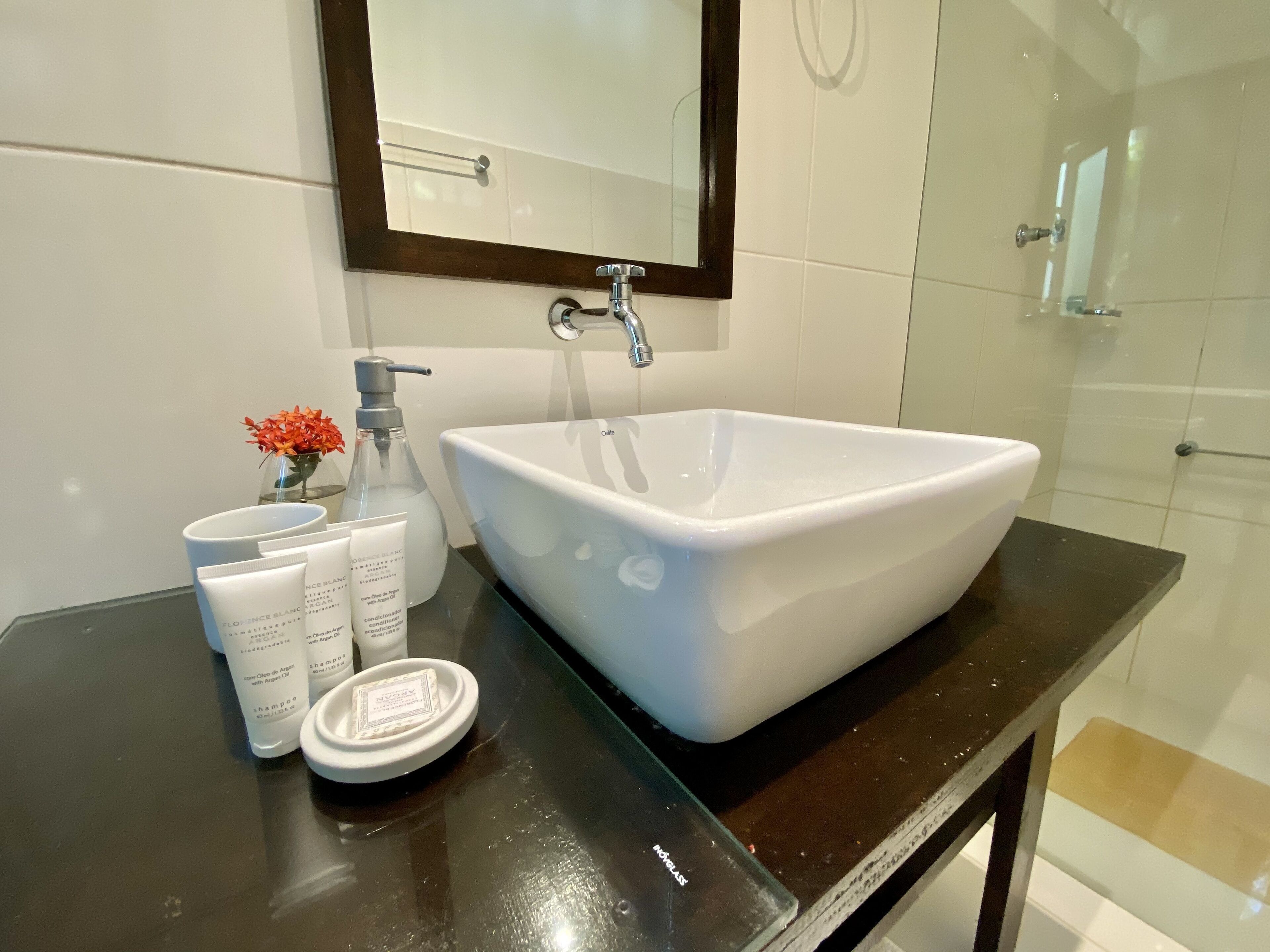 Ein Badezimmer mit einem weißen Waschbecken, einem Spiegel und Toilettenartikeln auf einer schwarzen Ablagefläche.
