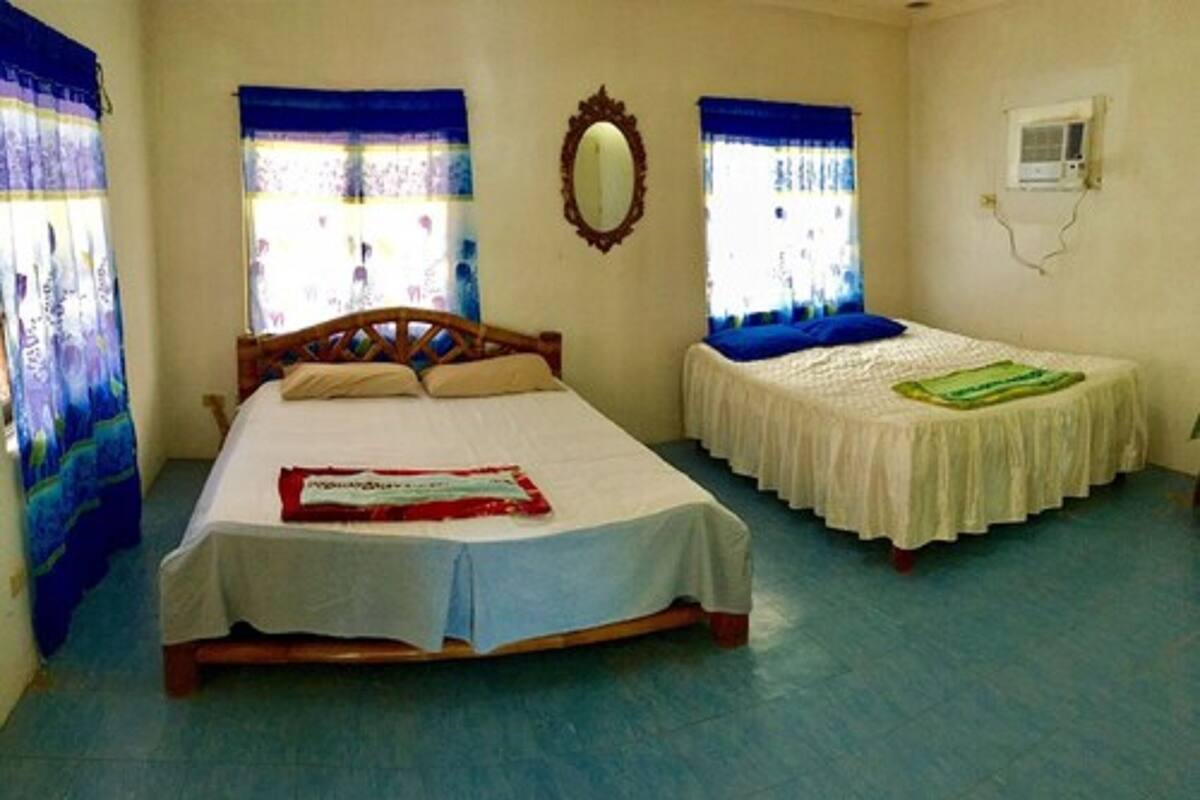 A bedroom with a large bed, a smaller bed, a mirror, and a window with curtains.