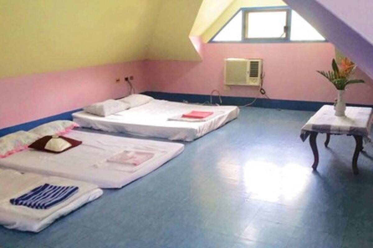 A room with three beds, a small table with a vase, and a window.