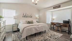 Un dormitorio con cama, mesitas de noche, un escritorio y una silla.