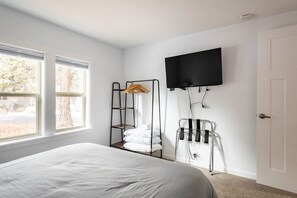 Une chambre Ă coucher avec un lit, un tĂ©lĂ©viseur fixĂ© au mur, une fenĂȘtre et une porte.