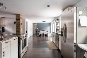 A modern kitchen with stainless steel appliances, a dining area with a table and chairs, and a hallway leading to another room.