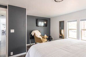 Hotellihuone, jossa on suuri sänky, seinälle asennettu televisio, tuoli ja pieni pöytä.