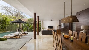 Un espacio interior moderno con piscina, sillones de descanso, zona de comedor y televisor.