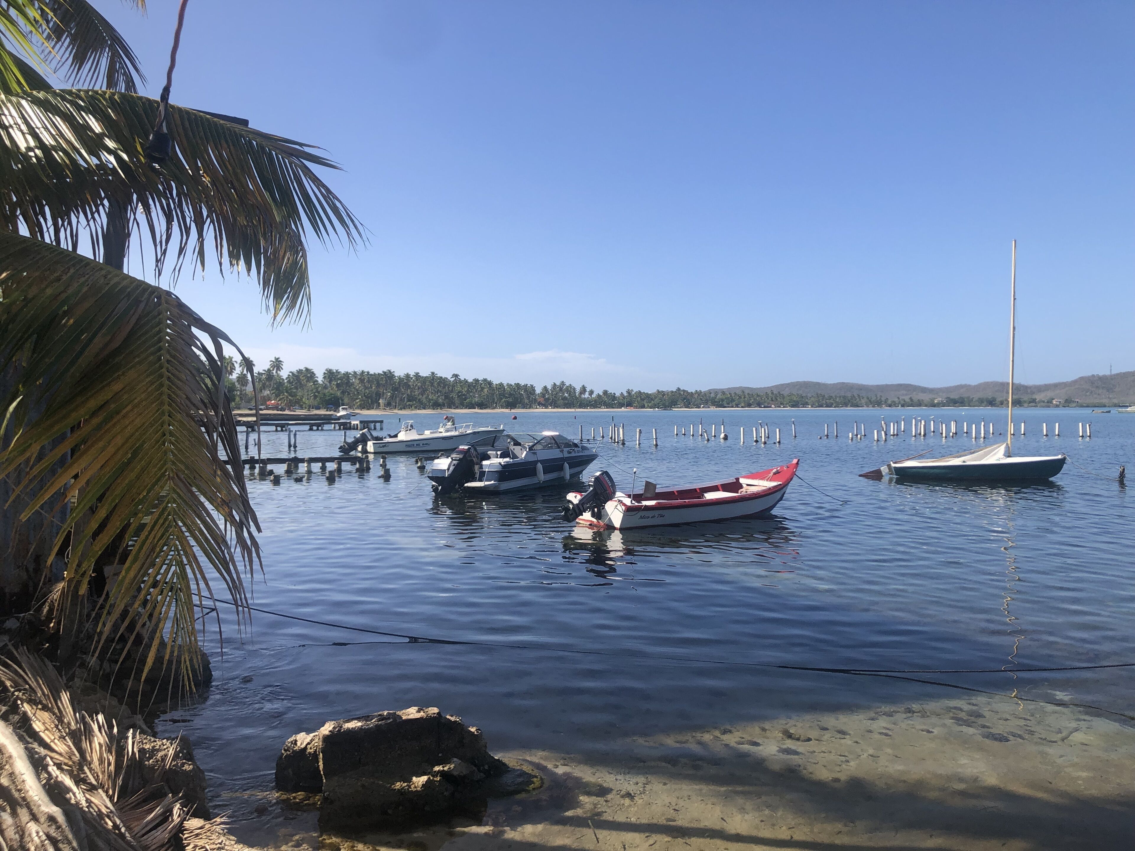 Un port tranquil amb vaixells amarrats, una platja sorrenca i un cel serè.