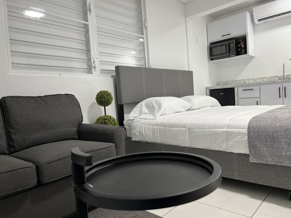 A modern hotel room with a grey sofa, a round black table, a neatly made bed, and a small potted plant. - Unique brand new apartment inside Poblado Boqueron (Boquerón)