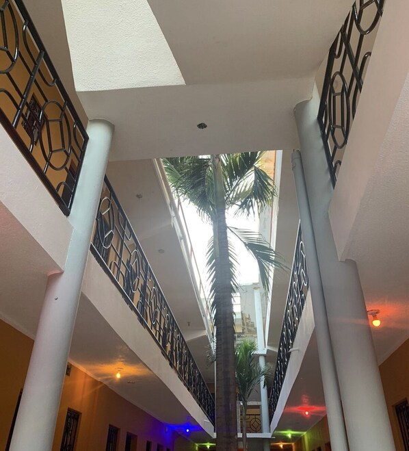 Un atrium à plusieurs niveaux, avec un palmier au centre, des piliers blancs et des rampes décoratives en métal.