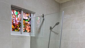 Une cabine de douche fermée par des parois en verre, dotée d’un pommeau de douche à main et d’un robinet fixé au mur.