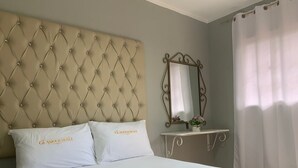 Une chambre d’hôtel avec une tête de lit capitonnée, deux oreillers blancs portant la mention « GLAMOUR HOTEL », une table de chevet avec un miroir et un couvre-lit blanc.