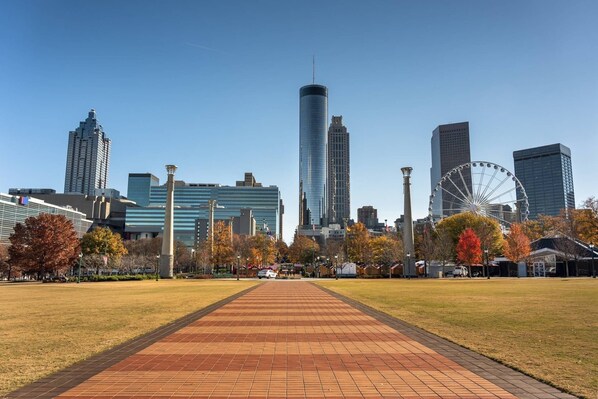 Un paisaje urbano con edificios modernos, una noria y un parque central con un sendero pavimentado.
