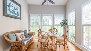 A dining area with wicker furniture, a ceiling fan, and large windows with blinds. - Experience the Private Pond & Dock |Relax by the Fire |Raving Reviews at Blackjack Acres|Truist Park (Marietta)
