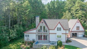 A two-story house with a stone facade, red trim, and a garage. - Experience the Private Pond & Dock |Relax by the Fire |Raving Reviews at Blackjack Acres|Truist Park (Marietta)
