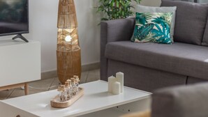 A modern living room with a white coffee table, a tall bamboo lamp, and a grey sofa with a tropical leaf pillow.