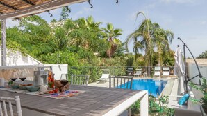 A poolside area with a table set for two, surrounded by lush greenery and a clear blue pool.