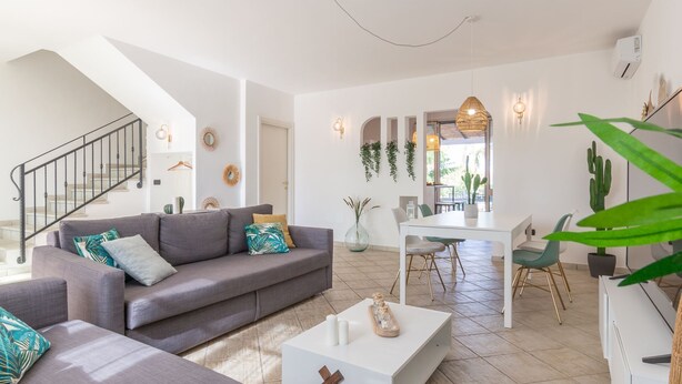 A modern living room with a grey sofa, a coffee table, and a dining area with a white table and chairs.