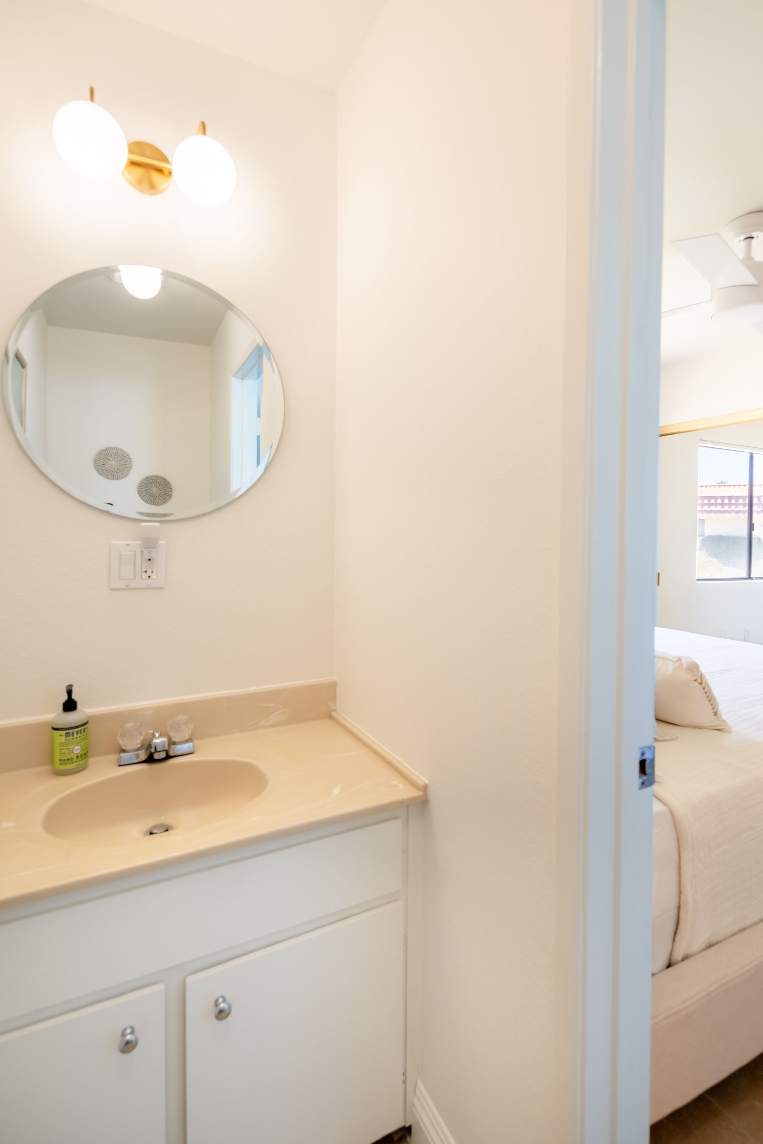 A bathroom with a round mirror, a sink, and a window.