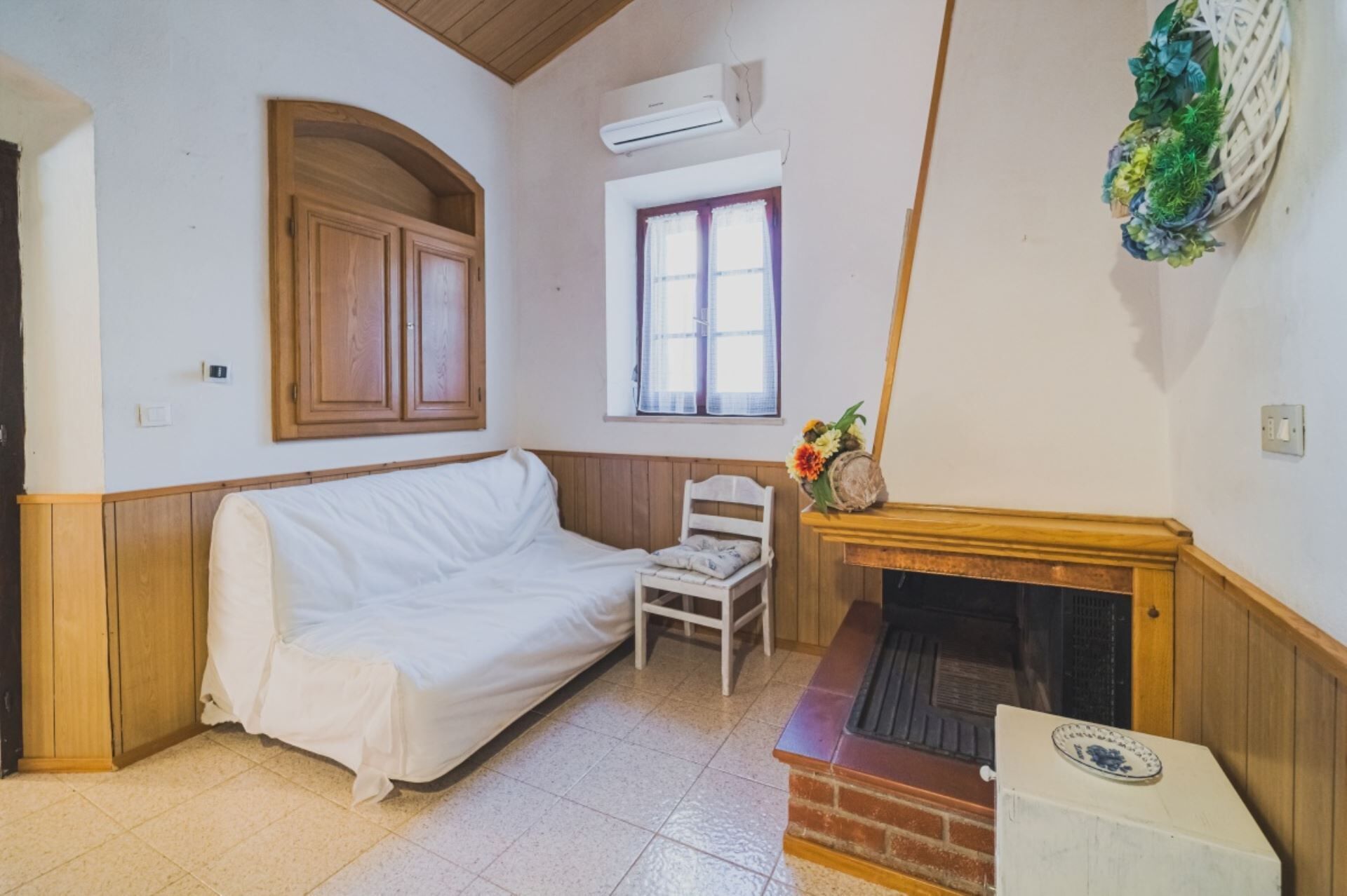 A room with a white sofa, a wooden cabinet, a fireplace, and a window with curtains.