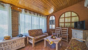 A cozy living room with a wooden ceiling, a sofa, a chair, a small table, and a television. - UN GIARDINO SU PARETI (Capoliveri)
