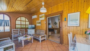 A cozy room with wooden walls and a tiled floor, featuring a sofa, chairs, a small table, and a television. - UN GIARDINO SU PARETI (Capoliveri)