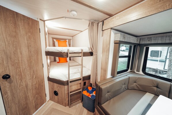 Ein kompaktes Wohnmobil-Interieur mit einem Schlafsteig, einer gepolsterten Sitzecke und einem Fenster mit Ausblick.