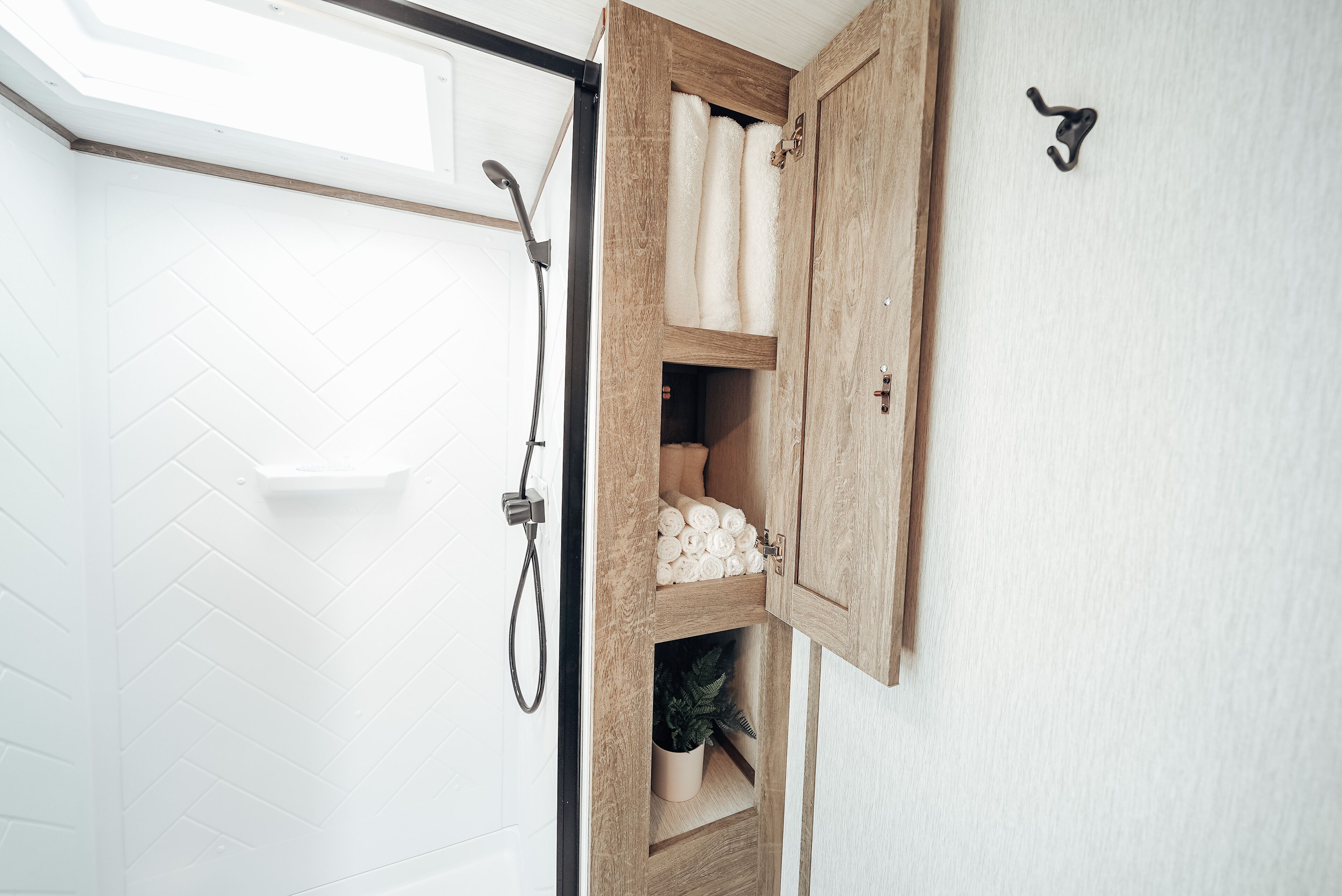 Ein Badezimmer mit einem Holzkabinett, das Handtücher und einen Blumentopf beinhaltet.