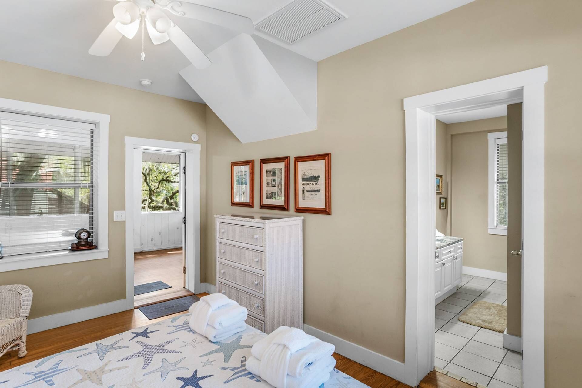 Quarto com ventilador de teto, penteadeira branca, porta que dá para outro cômodo e tapete com padrão de estrelas.