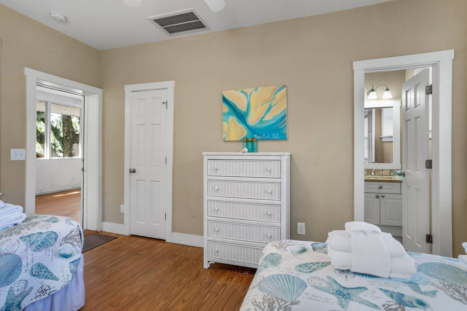 A bedroom with a bed, a dresser, a painting, and a bathroom visible through an open door.