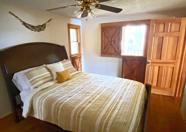 A bedroom with a bed, a ceiling fan, a wooden door, and a window. - Secluded SW Michigan Lake View Log Cabin w/ Fire Pit & Deck on Long Lake (Colon)