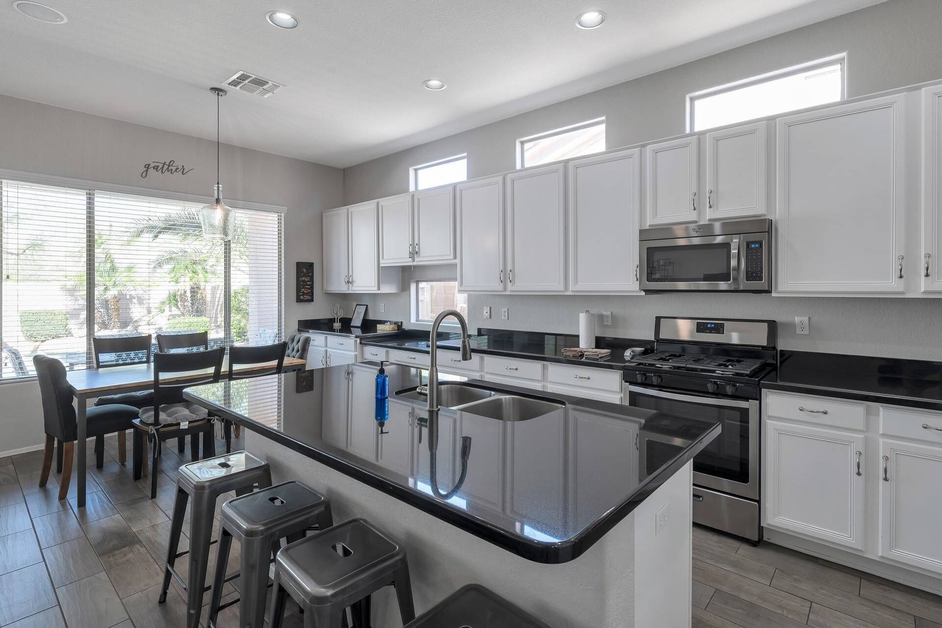 A modern kitchen with white cabinets, a central island with stools, a stainless steel sink, and a built-in microwave.
