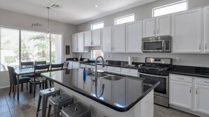 A modern kitchen with white cabinets, a central island with stools, a stainless steel sink, and a built-in microwave. - Great Location w/ Private Heated Pool, Near Hiking/Golfing/Shopping/Dining & Mayo Clinic + FREE GOLF (Phoenix)