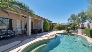 A swimming pool with a curved edge, surrounded by a patio area with outdoor furniture and palm trees. - Great Location w/ Private Heated Pool, Near Hiking/Golfing/Shopping/Dining & Mayo Clinic + FREE GOLF (Phoenix)