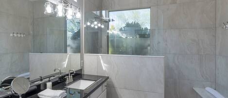 A modern bathroom with a large mirror, a sink with a vanity, and a shower area.