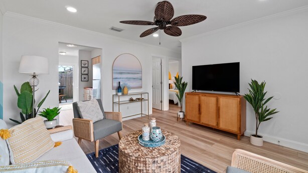 Ein modernes Wohnzimmer mit Deckenventilator, Fernseher und Essbereich mit Meerblick.