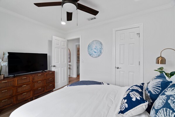 A bedroom with a large bed, a TV on a wooden dresser, a ceiling fan, and a round wall decoration.