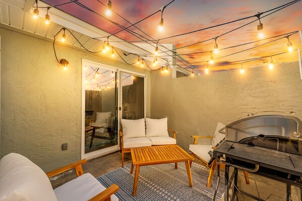 Une terrasse extérieure équipée d’un barbecue, d’un espace salon et de guirlandes lumineuses.