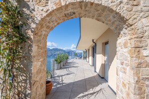 Ein Steingewölbe führt zu einem Balkon mit Blick auf Berge und ein Gewässer.