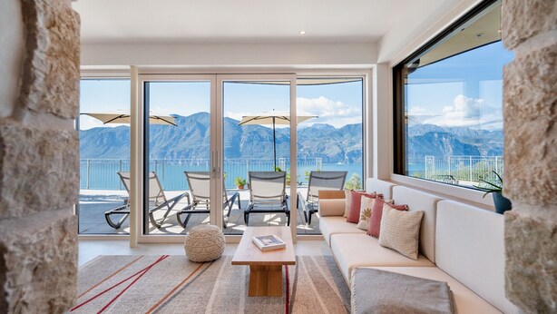 Ein modernes Wohnzimmer mit Sofa, Couchtisch und Sesseln, mit Blick auf eine malerische Berglandschaft durch große Fenster.