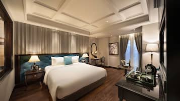 A hotel room with a large bed, a nightstand with a lamp, a dresser, and a view of the city through the window.