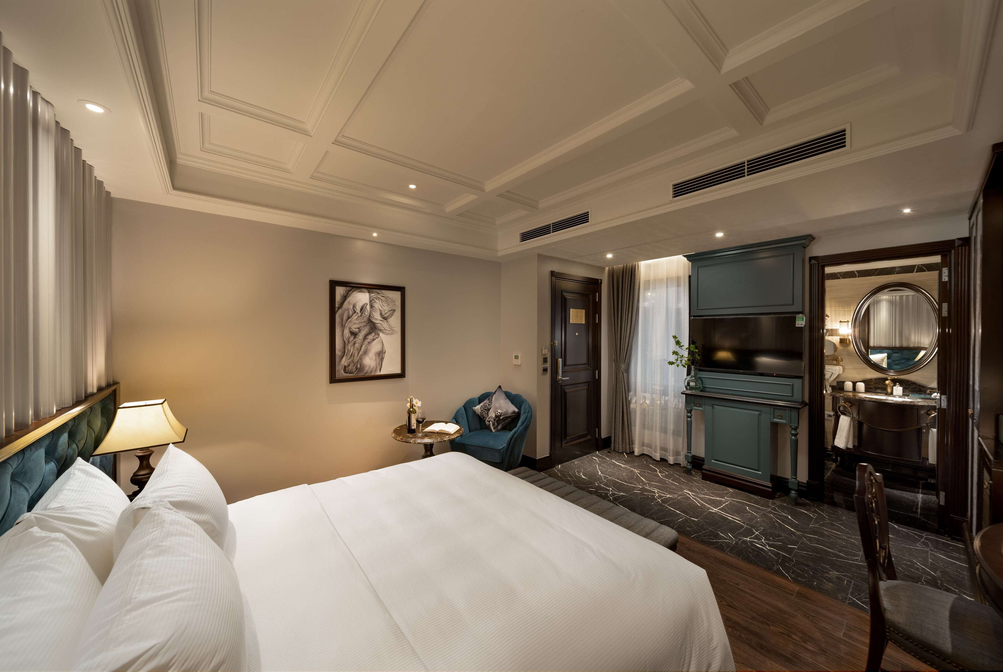 Une chambre d’hôtel avec un grand lit, un bureau, une chaise, une salle de bain avec un miroir et une porte donnant sur une autre pièce.