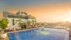 A rooftop swimming pool with lounge chairs and palm trees, surrounded by a modern building with large glass windows. - Meritel Hanoi (Hanoi)