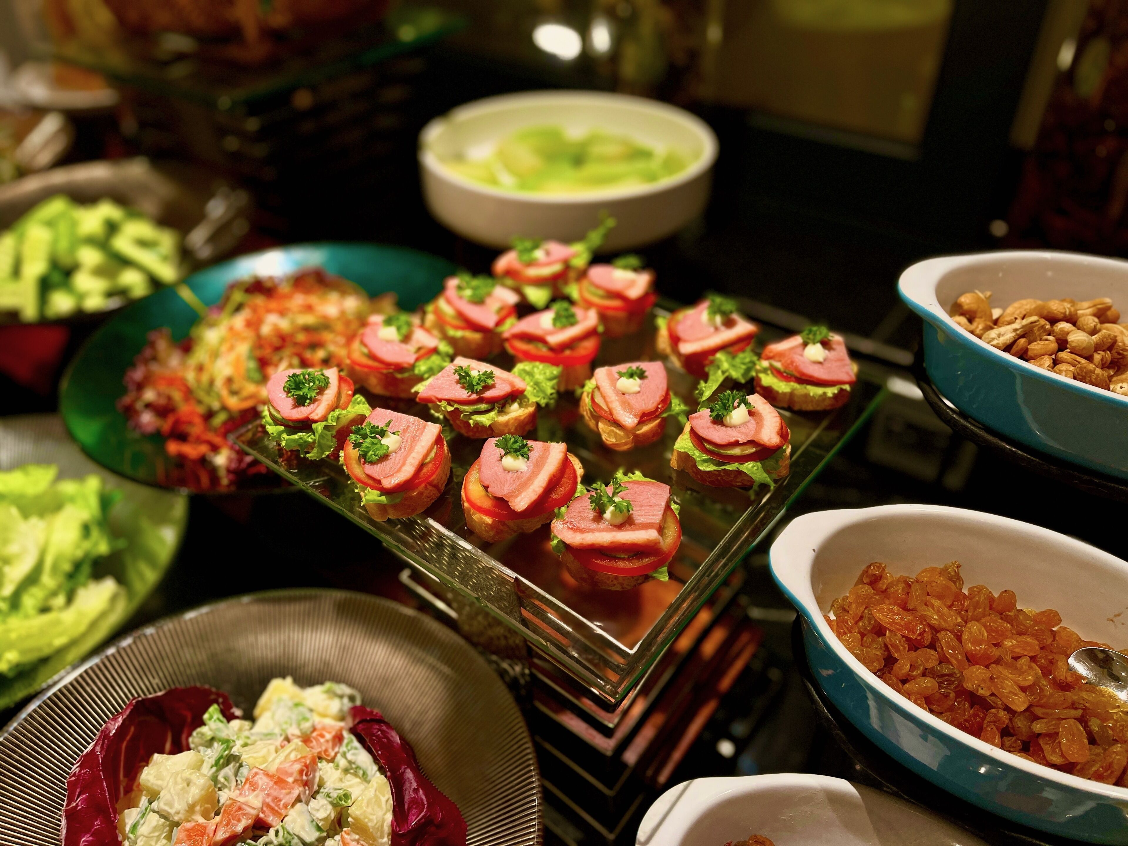 Un bufé con diversos platos, incluyendo una bandeja de aperitivos, un bol de ensalada y un bol de nueces.