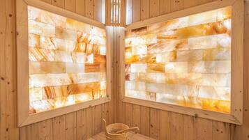 Uma sauna de madeira com um banco, um balde e uma janela com vista para o interior da sauna.