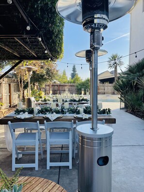 Un patio al aire libre con una lámpara de mesa metálica, sillas blancas y una mesa dispuesta para comer.